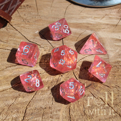 Set of pink polyhedral dice on a wooden surface with 'roll with it' text.