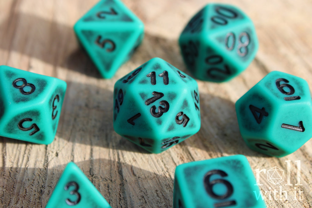 Matte teal polyhedral roleplaying dice set with black letters on a wooden surface