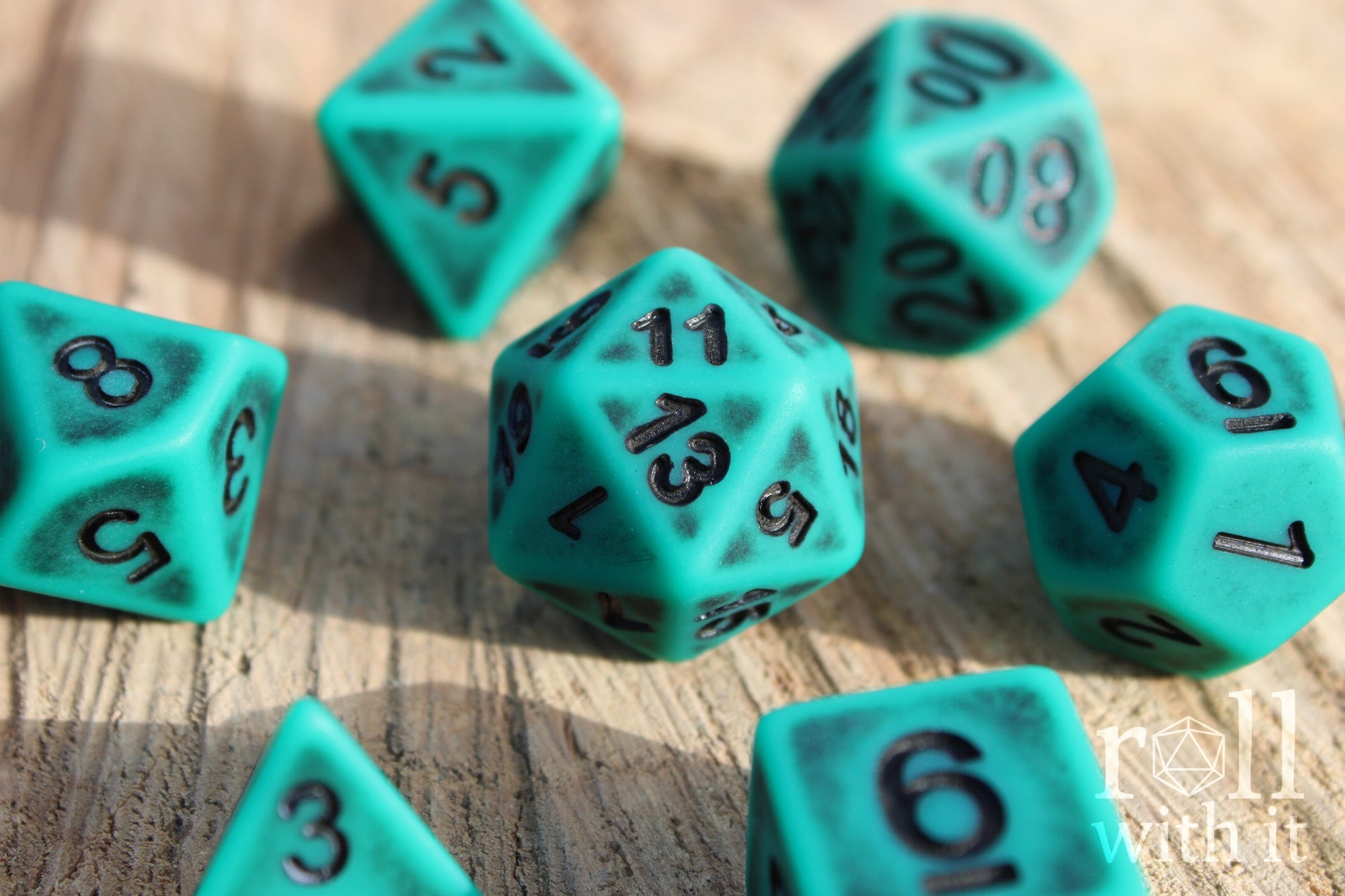 Matte teal polyhedral roleplaying dice set with black letters on a wooden surface