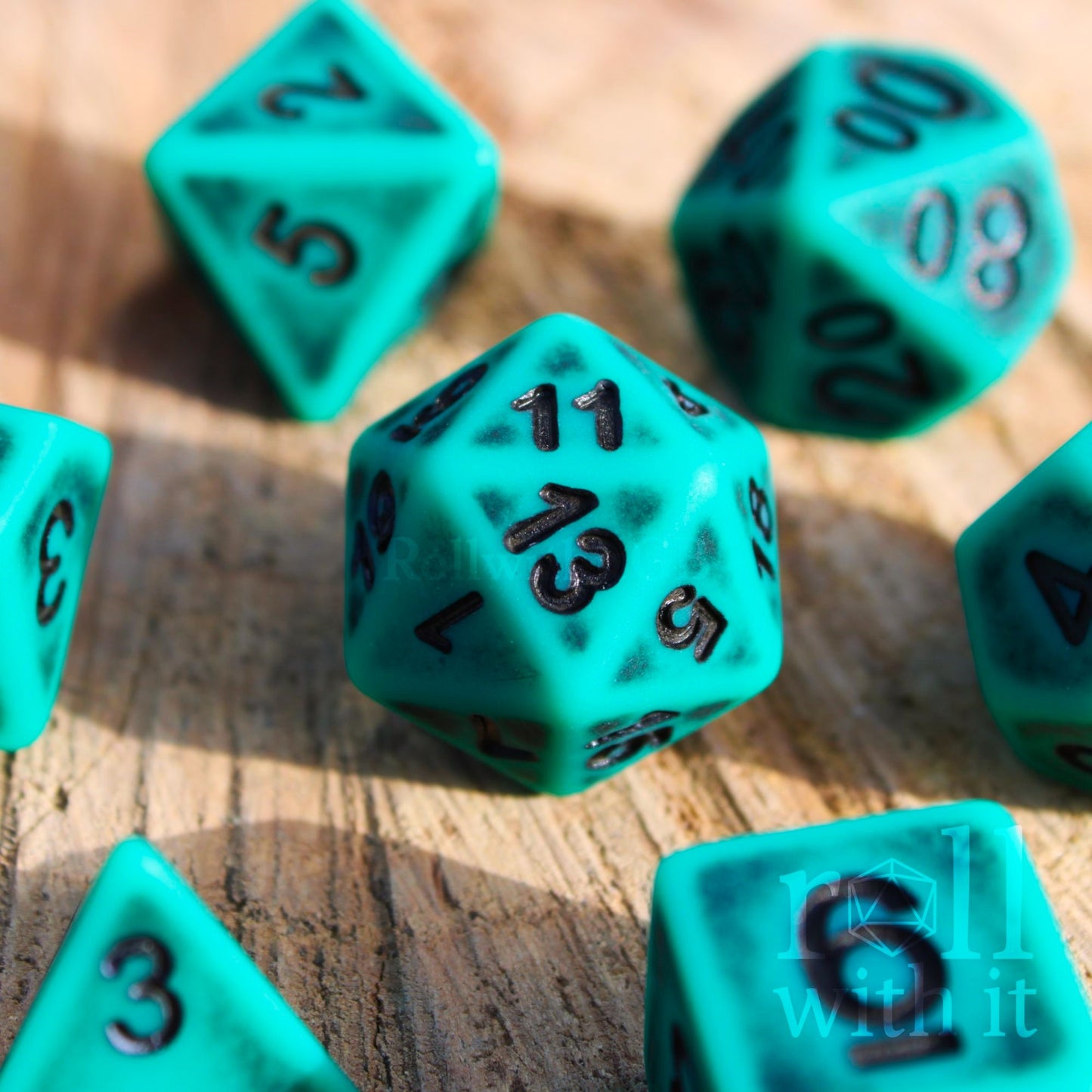 Turquoise matte worn polyhedral dice with black numbers on a wooden surface