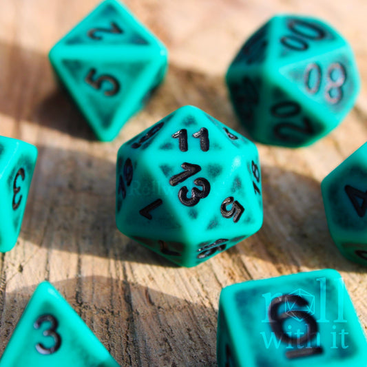Turquoise matte worn polyhedral dice with black numbers on a wooden surface