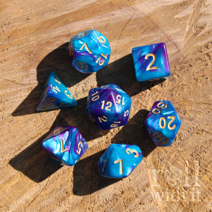 Set of bright ultramarine blue and purple polyhedral dice with gold numbers on a wooden surface.