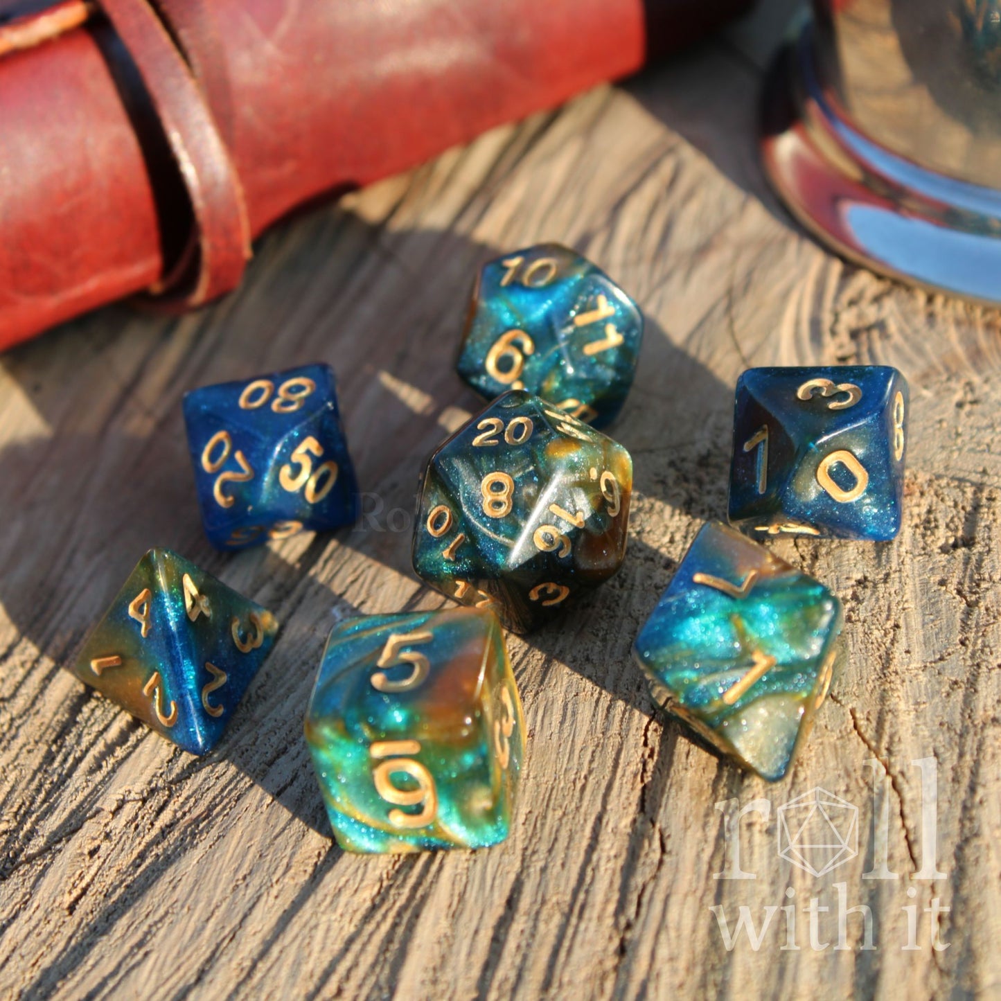 Set of mixed swirling blue and gold polyhedral dice on a wooden surface with 'roll with it' branding.
