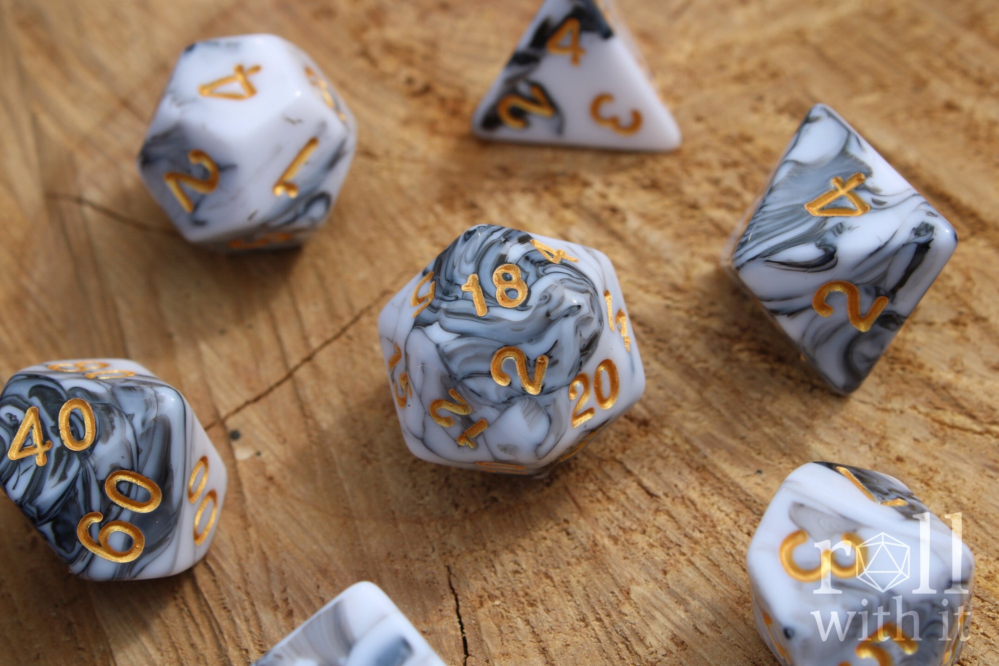 A set of creamy white and grey swirling polyhedral dice on a wooden surface