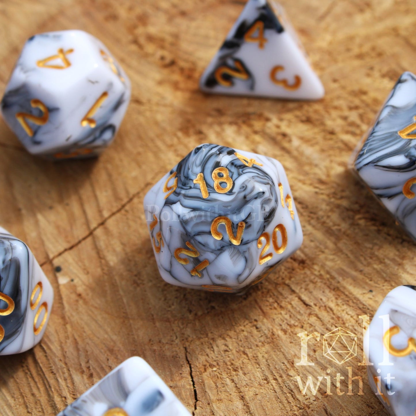 A set of creamy white and grey swirling polyhedral dice on a wooden surface