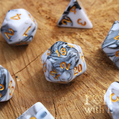 A set of creamy white and grey swirling polyhedral dice on a wooden surface