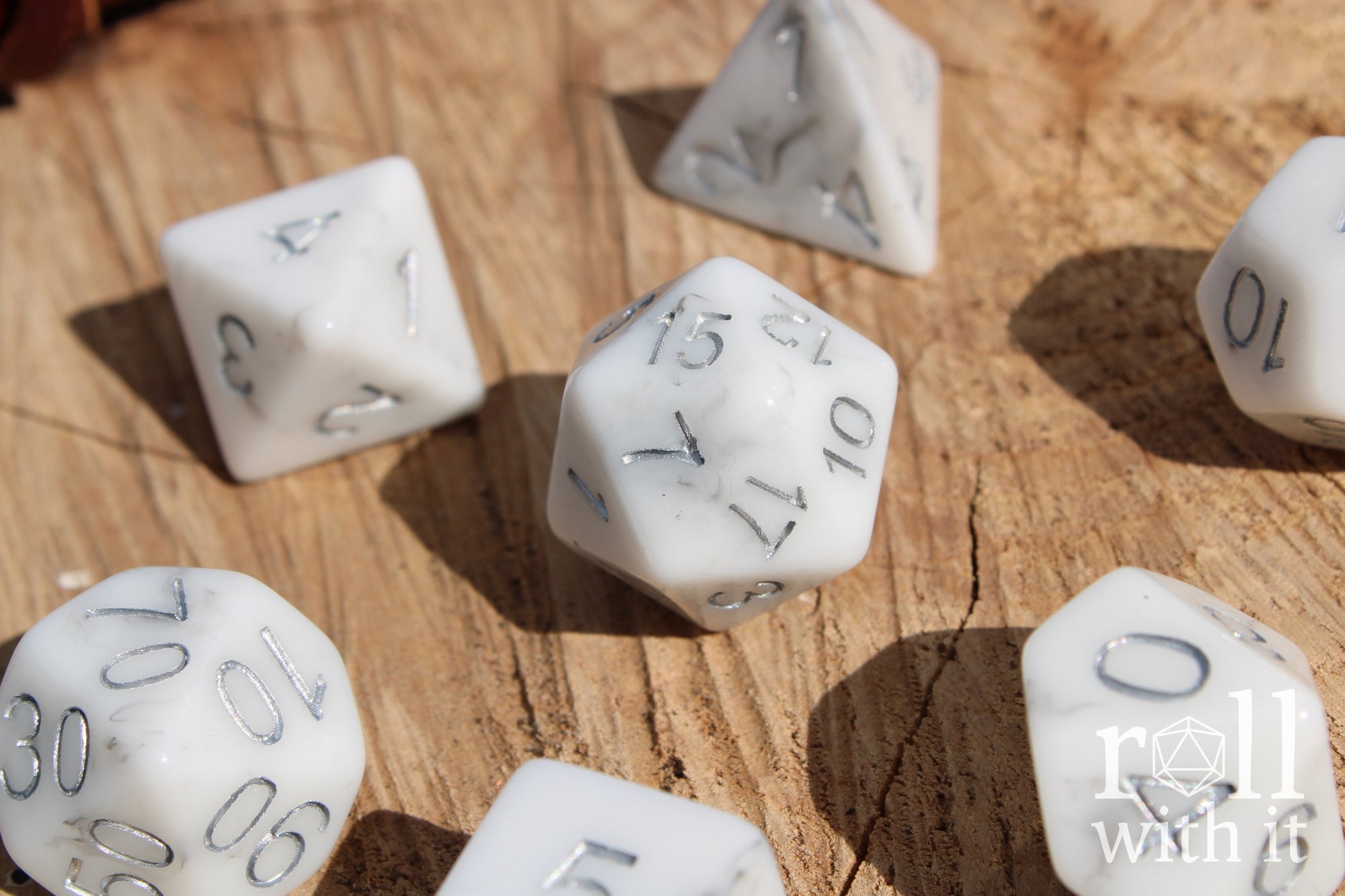 Granite White polyhedral roleplaying dice with silver numbers on a wooden surface