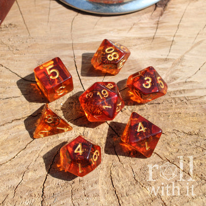 Set of amber-colored polyhedral dice with golden numbers and copper cogs inside on a wooden surface, featuring 'roll with it' branding.
