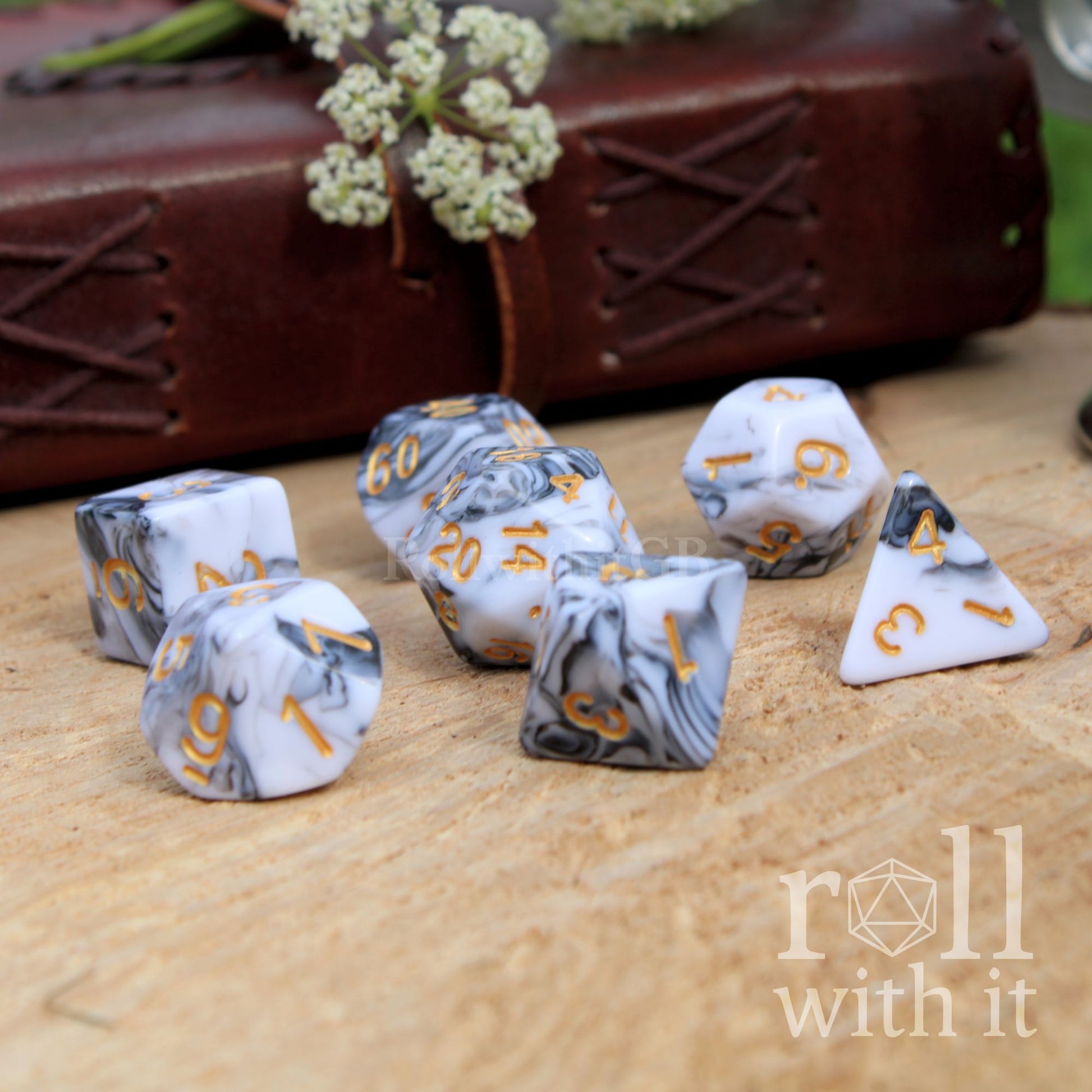 Set of dice with black grey and white marble pattern and gold numbers on a wooden surface, with 'roll with it' branding.