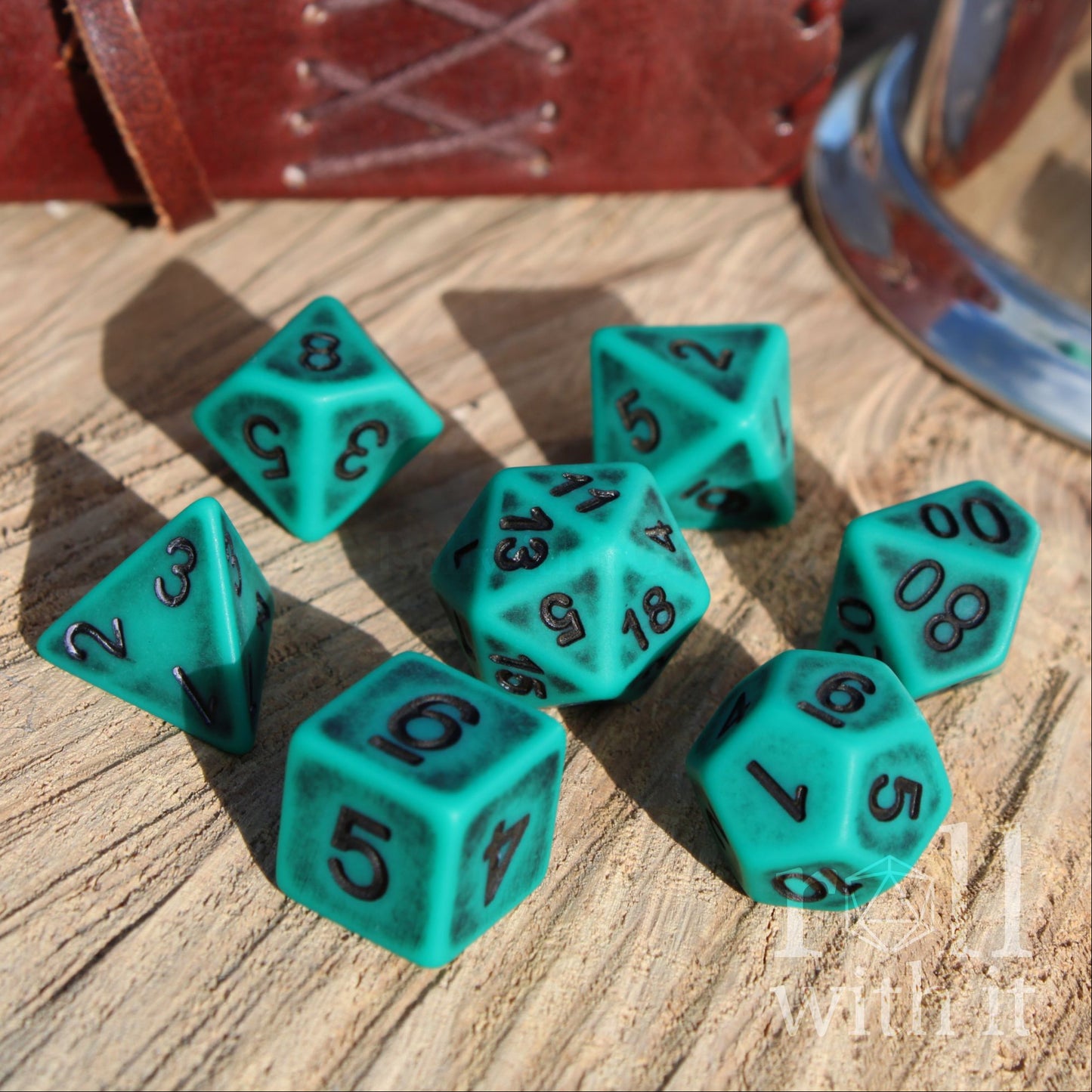 Set of matte teal polyhedral dice on a wooden surface with black numbers