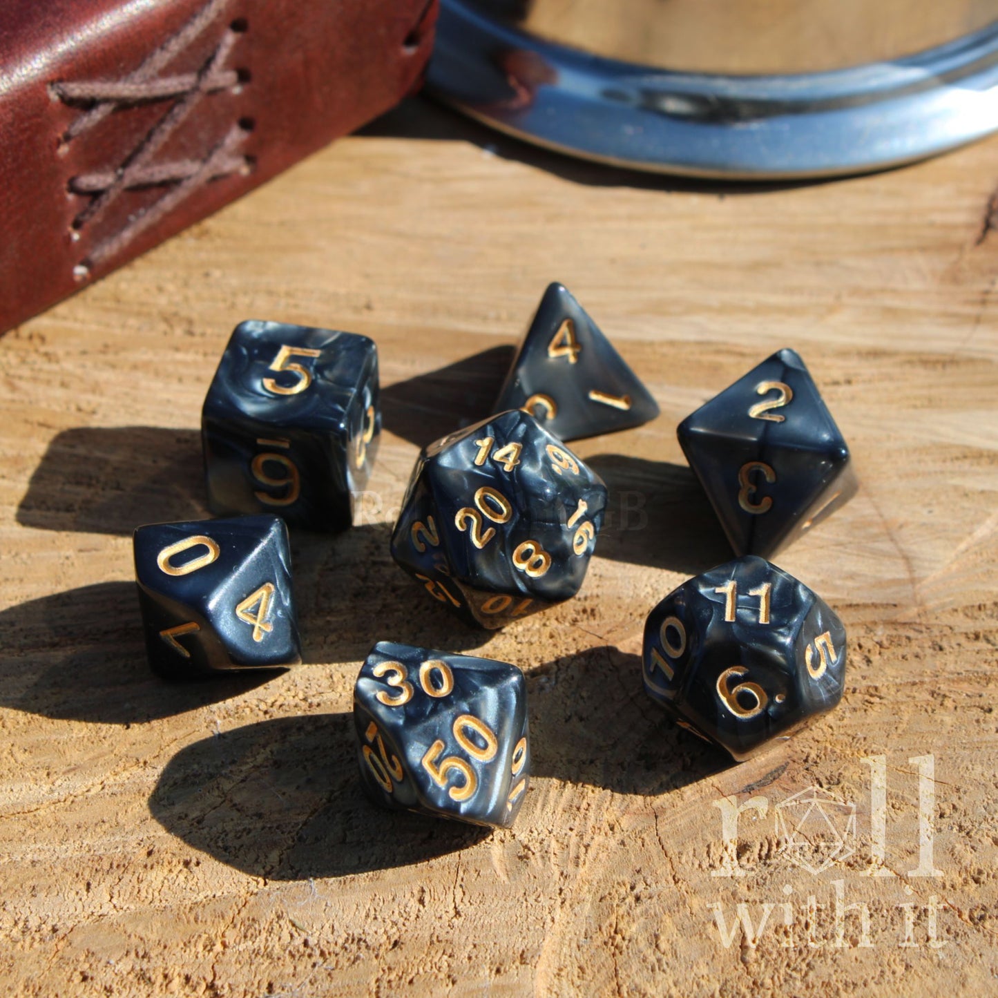 Swirling pearlescent shiny black dice with golden numbers of a wooden surface