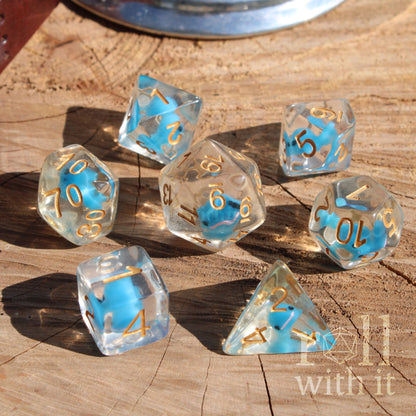 A set of 7 cute clear polyhedral dice with a mini whale inside on a wooden surface and with golden numbers