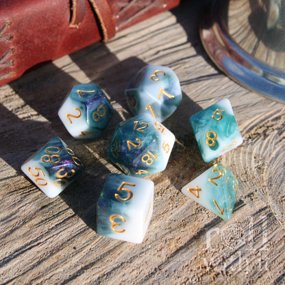 Set of 7 deep blue and white dice with gold numbers on a wooden surface