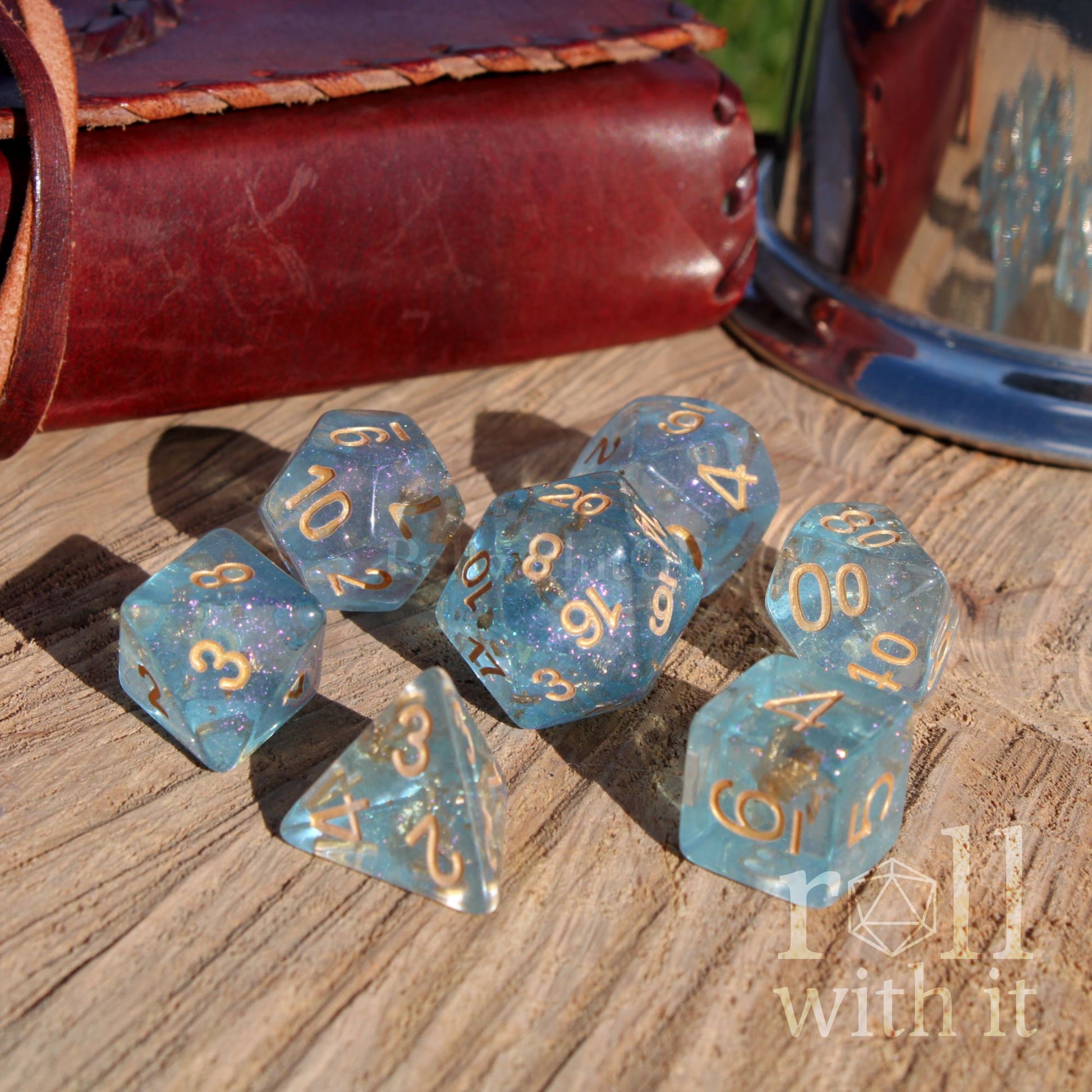 Set of blue bright polyhedral dice with gold numbers on a wooden surface, with a leather-bound book in the background.
