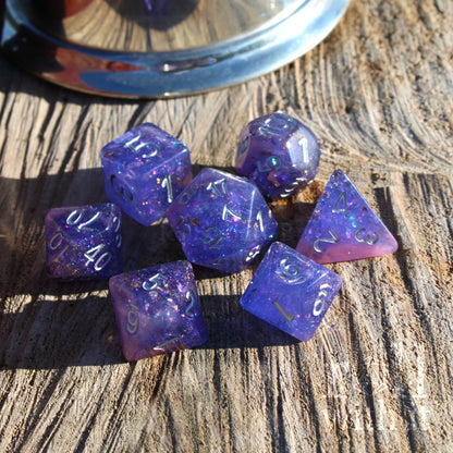 Set of purple pink mixed gold leaf silver numbered polyhedral dice on a wooden surface