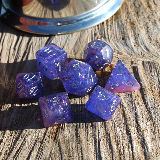 Set of purple pink mixed gold leaf silver numbered polyhedral dice on a wooden surface