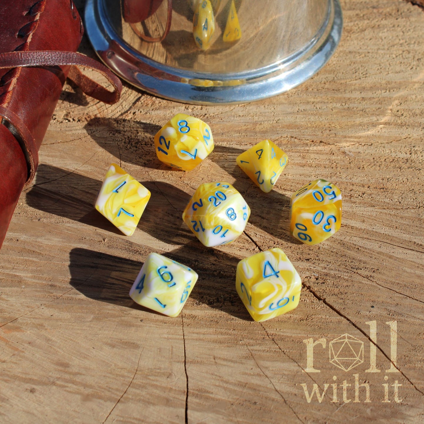 Yellow and white lemon sorbet coloured polyhedral dice with blue numbers on a wooden surface, featuring 'roll with it' branding.
