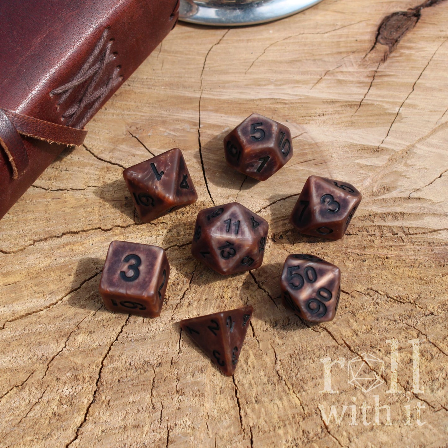 Set of metallic bronze polyhedral dice on a wooden surface with 'roll with it' text.