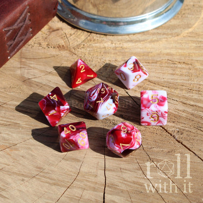 Set of red and white shiny TTRPG polyhedral dice on a wooden surface with 'roll with it' branding.