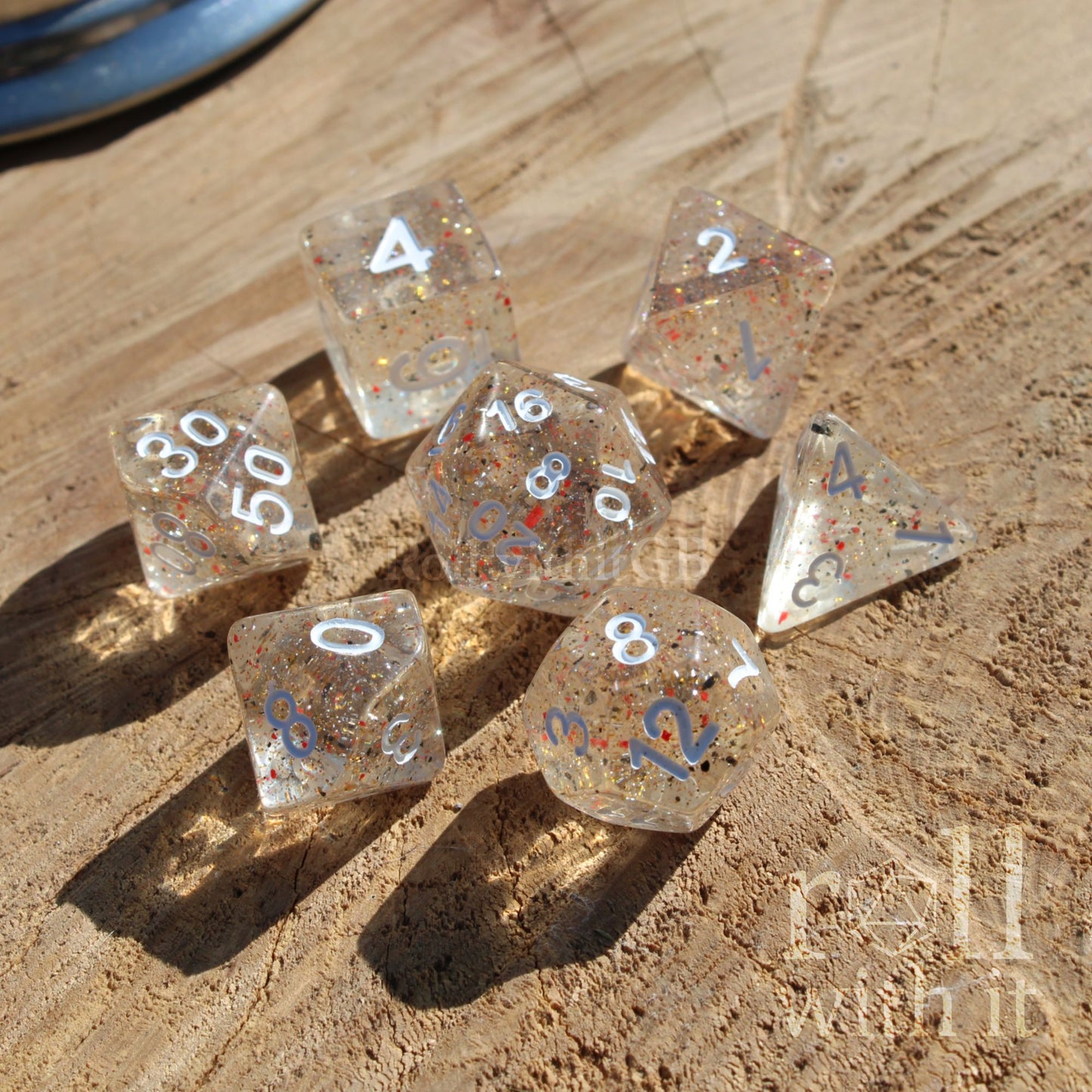 Set of clear polyhedral dice with glittery orange black insides and white numbers on a sandy surface