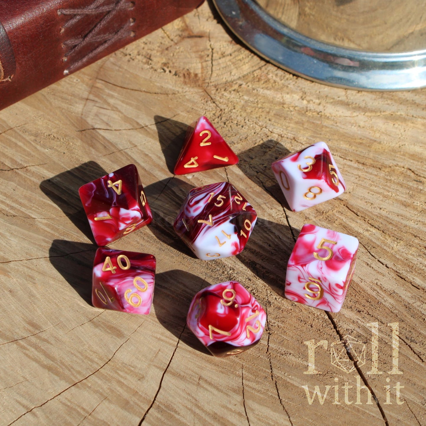 Set of mixed marble like pink and red polyhedral dice on a wooden surface with 'roll with it' text.