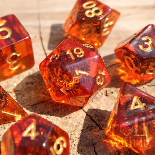 Transparent amber-colored polyhedral dice with gold numbers and copper cogs inside on a wooden surface.
