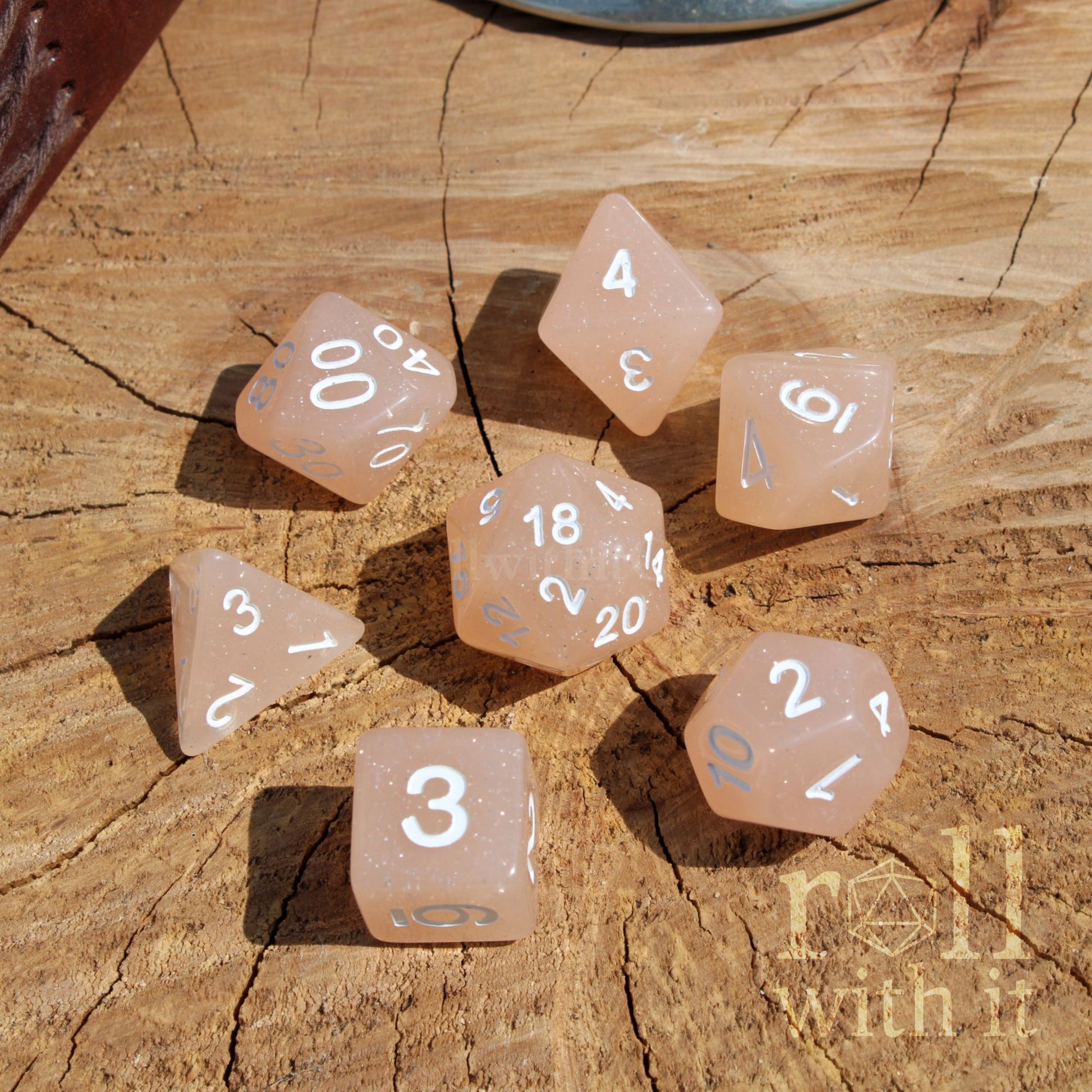 Set of pink beige dice with white numbers on a wooden surface, featuring the text 'roll with it'.