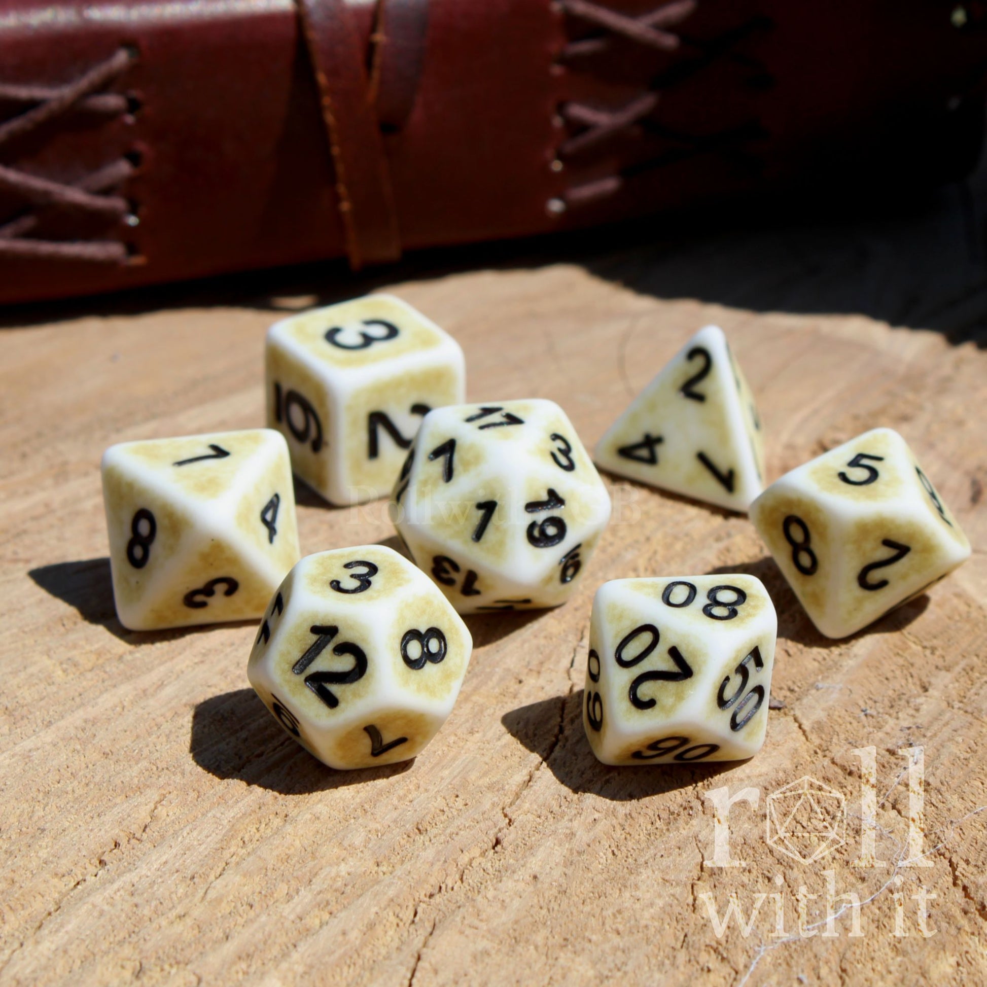 Side view of 7 matte bone white D&D polyhedral dice on a wooden surface
