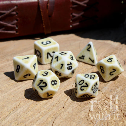 Side view of 7 matte bone white D&D polyhedral dice on a wooden surface