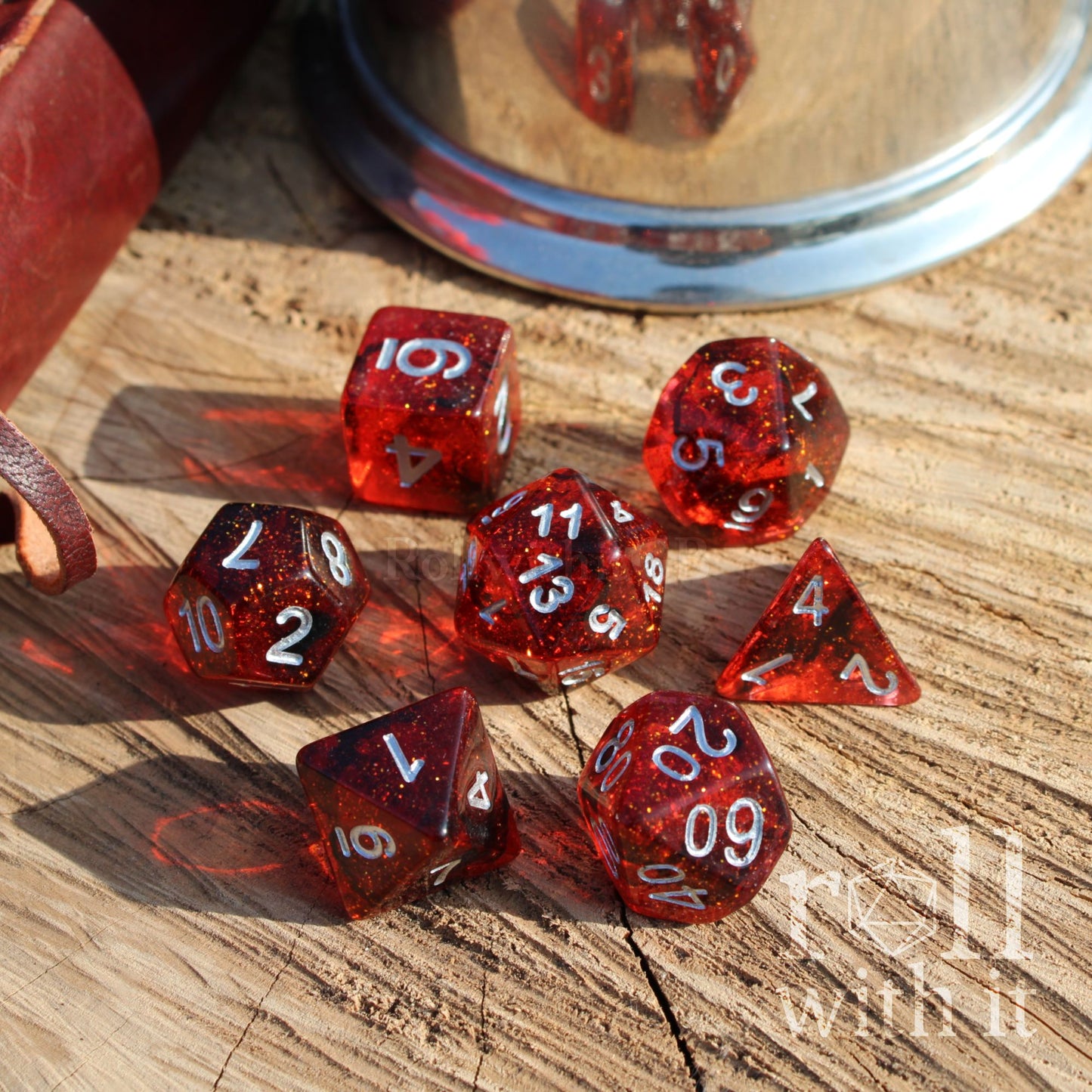 Top view of 7 polyhedral crimson red resin dice swirling and galaxy themed on a wooden surface