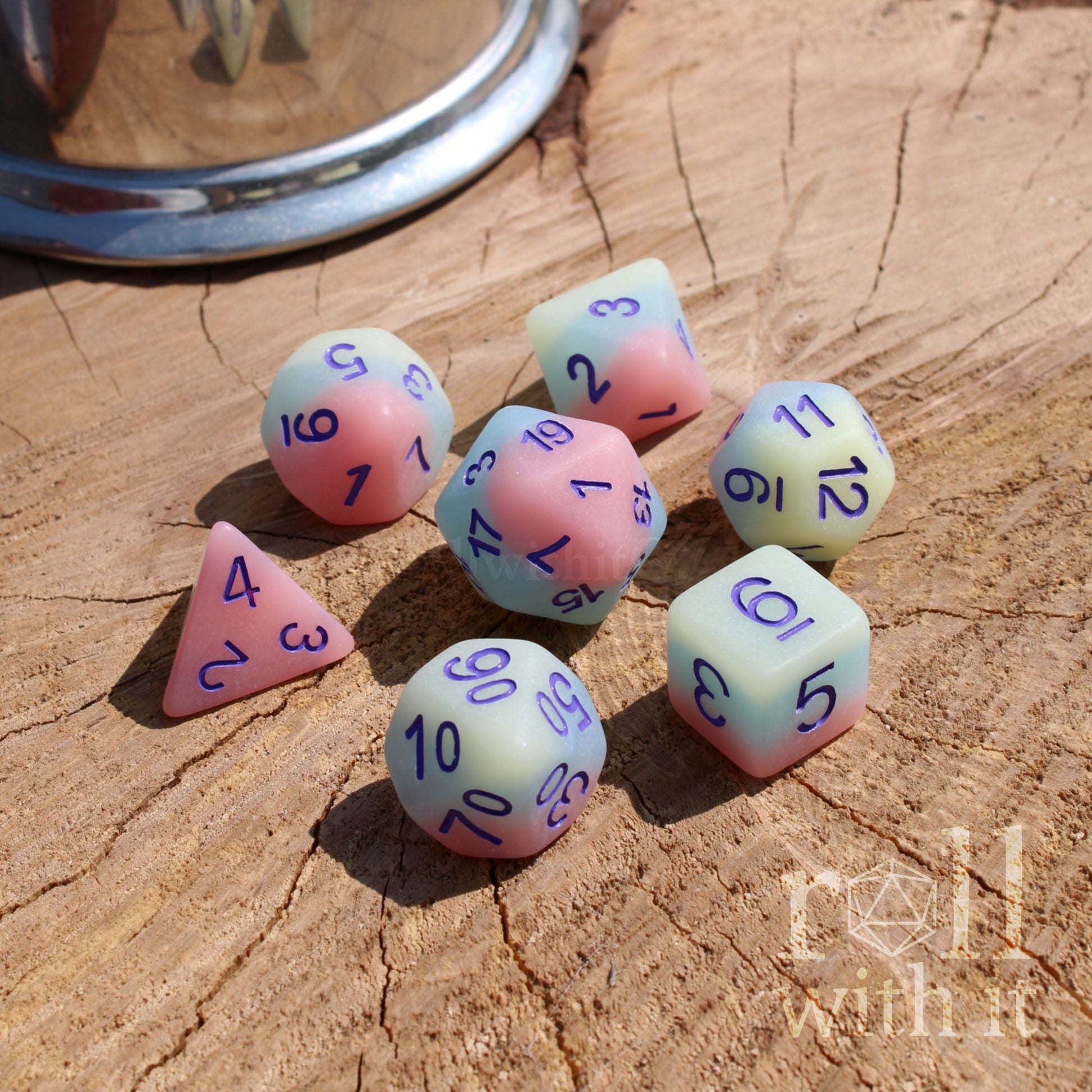Set of colorful polyhedral dice on a wooden surface with 'roll with it' branding.