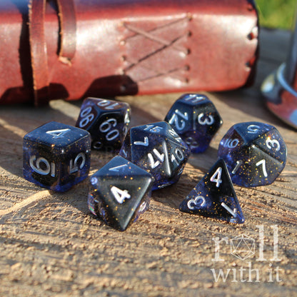 Set of blue and black dark starry glitter filled polyhedral dice on a wooden surface with 'roll with it' branding.