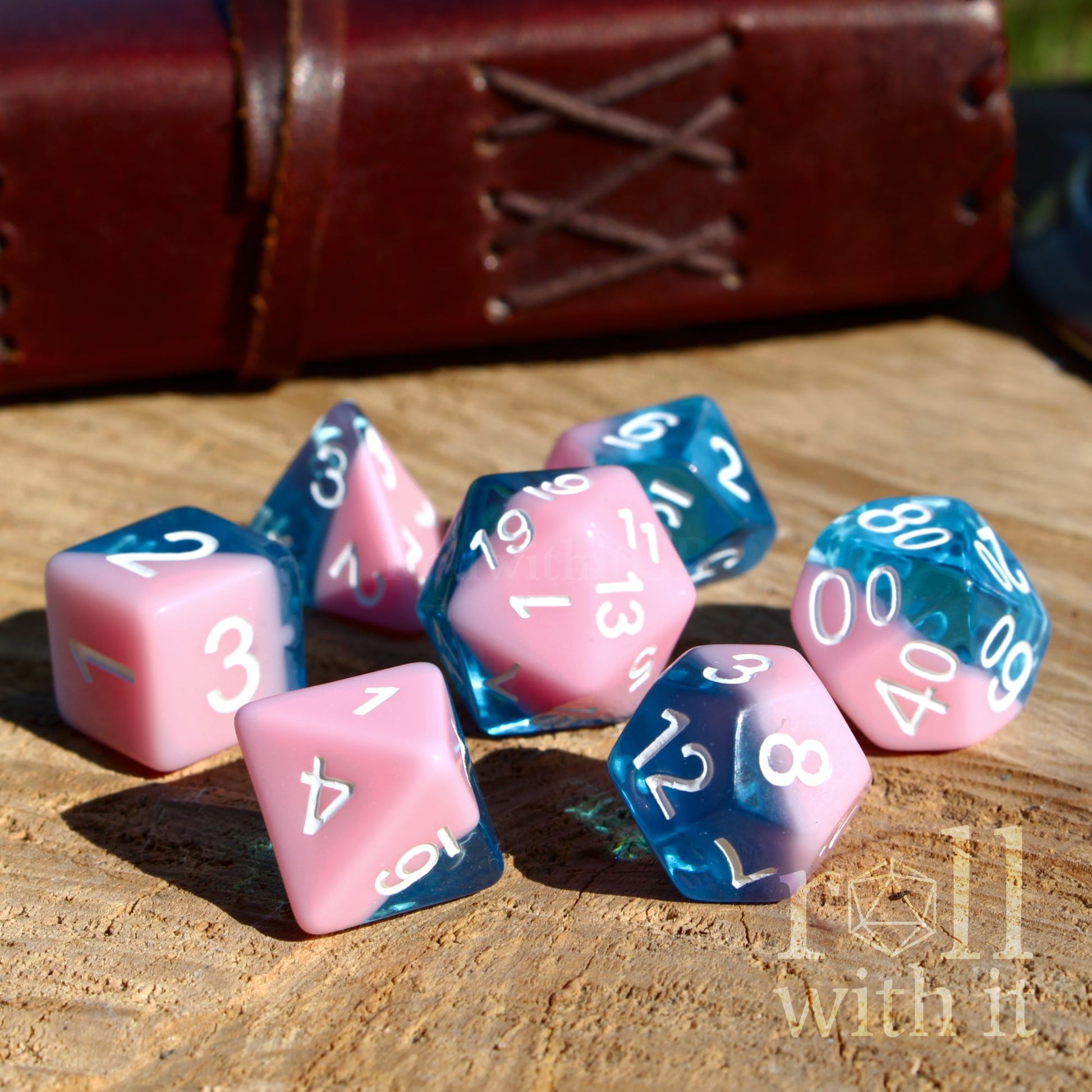 bright shiny pink and deep blue dice set on a wooden surface with a leather-bound book in the background.