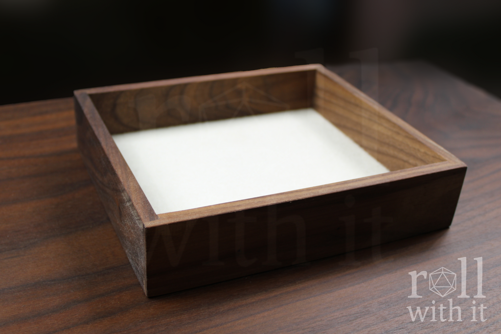 Wooden walnut dice tray with white felt interior on a wooden table, featuring 'roll with it' logo.