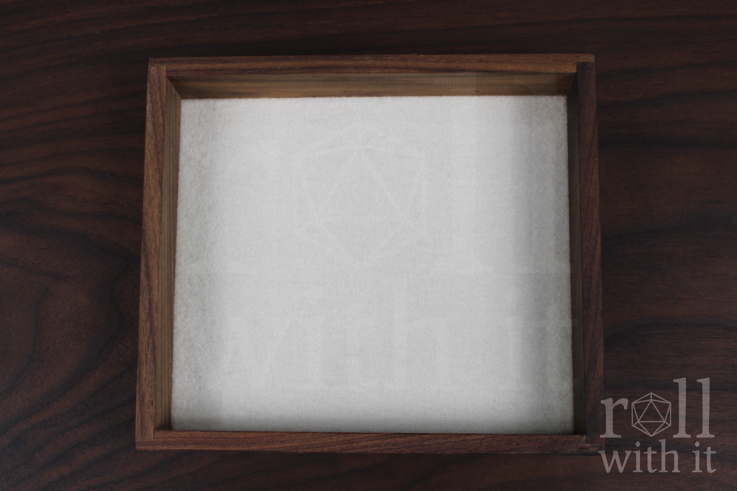 Wooden walnut dice tray with white felt interior on a wooden table, featuring 'roll with it' logo.