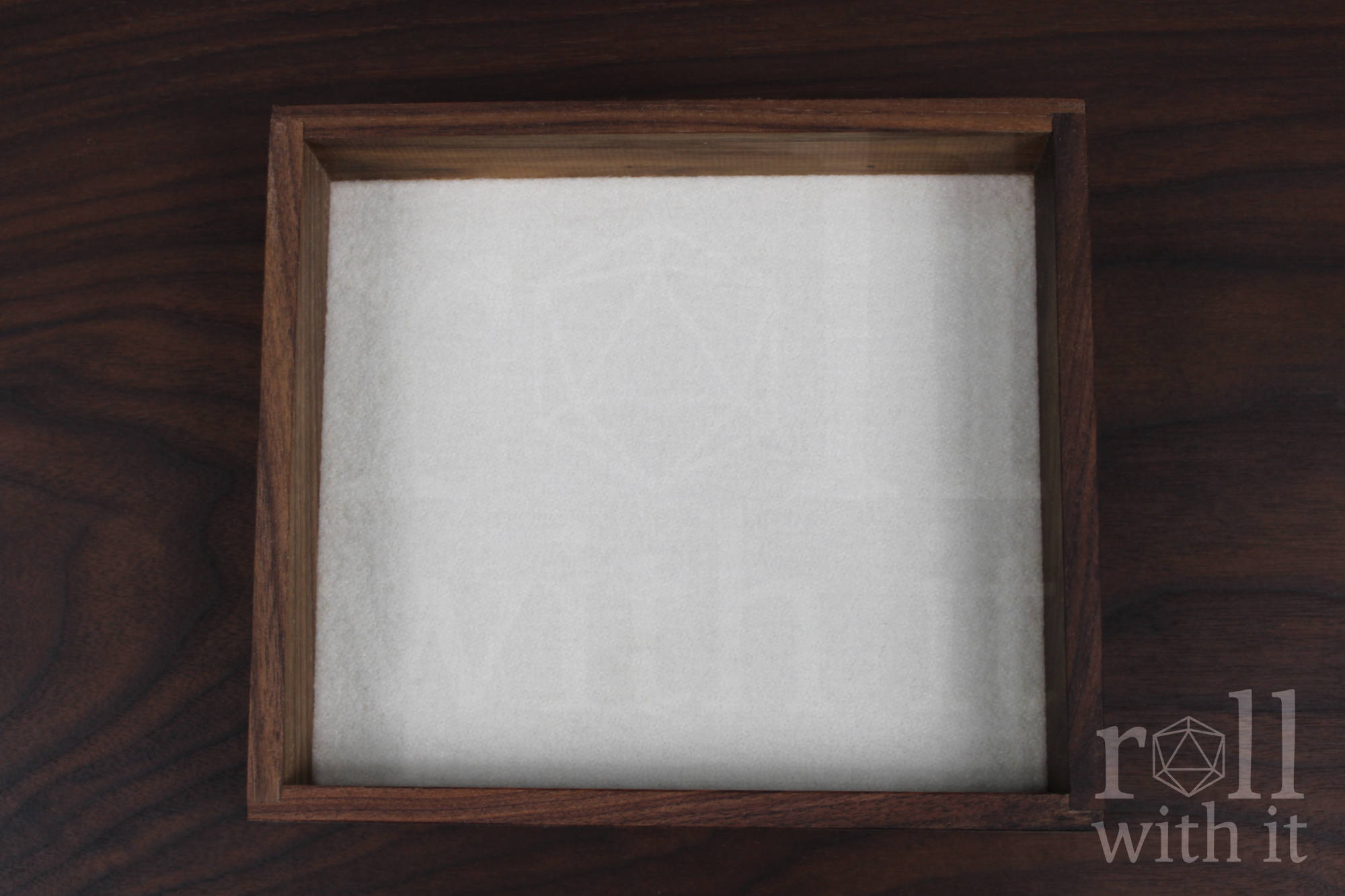 Wooden walnut dice tray with white felt interior on a wooden table, featuring 'roll with it' logo.