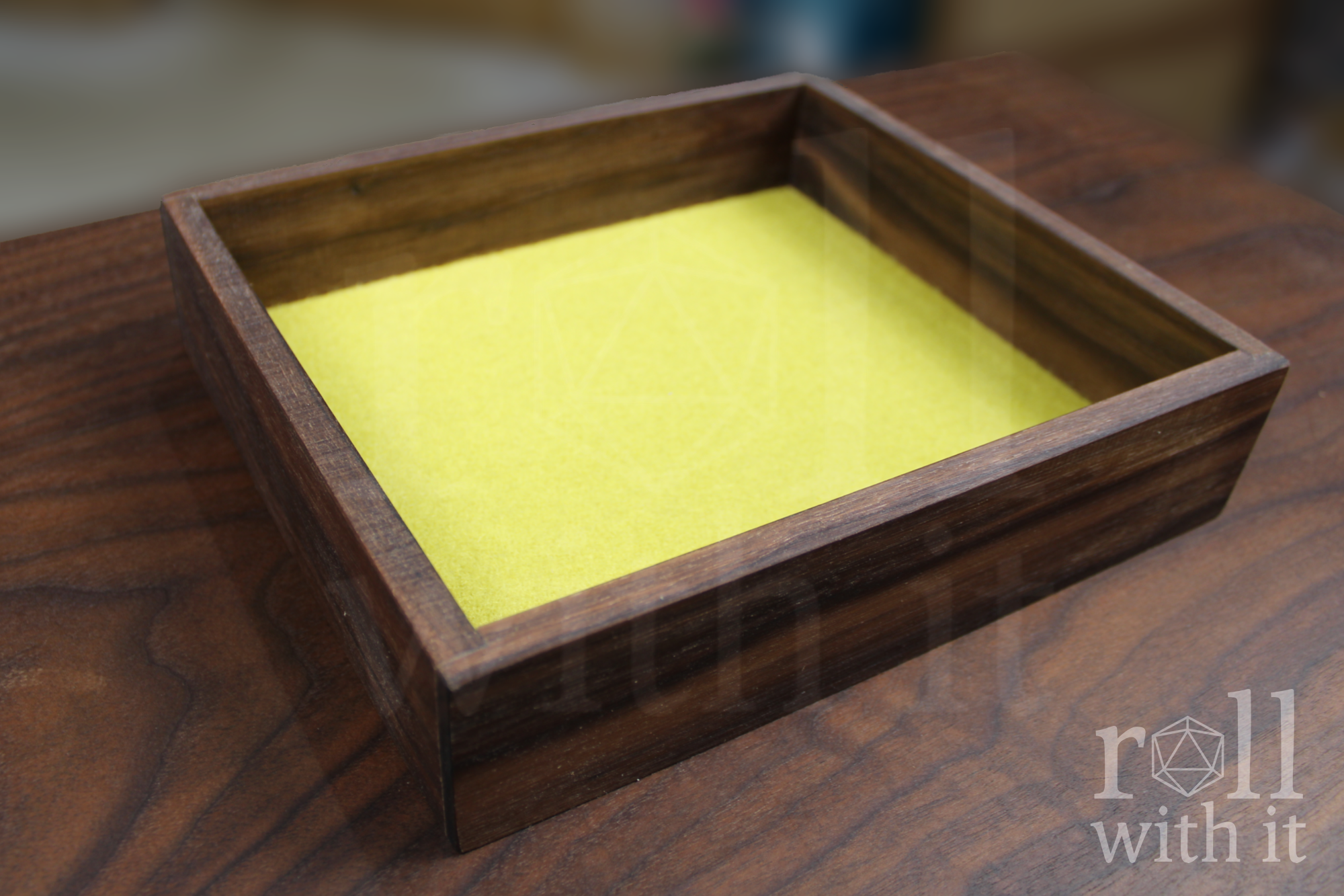 Solid walnut roleplaying dice tray with yellow felt interior sits on a wooden table. The image features a 'roll with it' logo.
