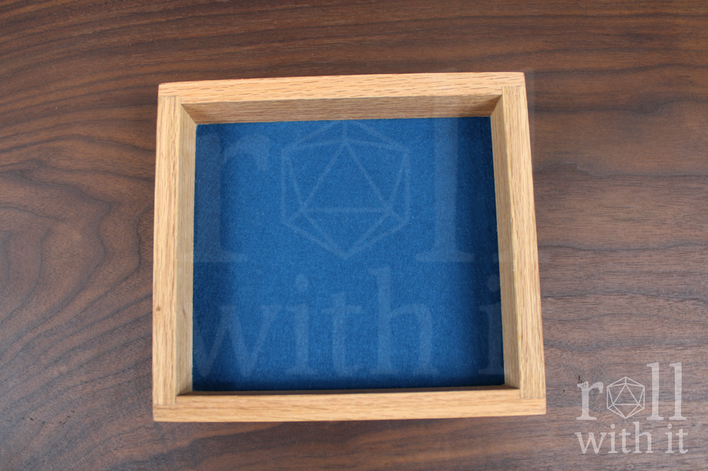 Wooden red oak dice tray with navy blue felt interior on a wooden table, featuring 'roll with it' logo.