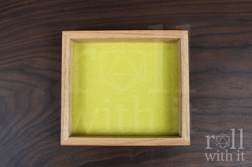Wooden red oak dice tray with chartreuse yellow felt interior base on a wooden walnut table. A featuring 'roll with it' logo sits in the bottom right corner.