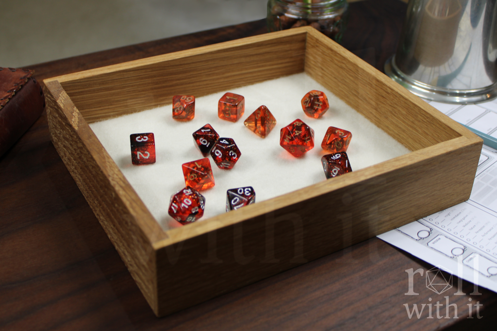 Orange, Red and black Dungeons and Dragons dice set in a wooden white oak tabletop dice tray on a table with 'roll with it' branding.