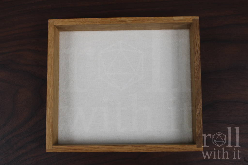An empty dungeons and dragons tabletop dice tray with a white felt base made from white oak wood sat on a wooden table