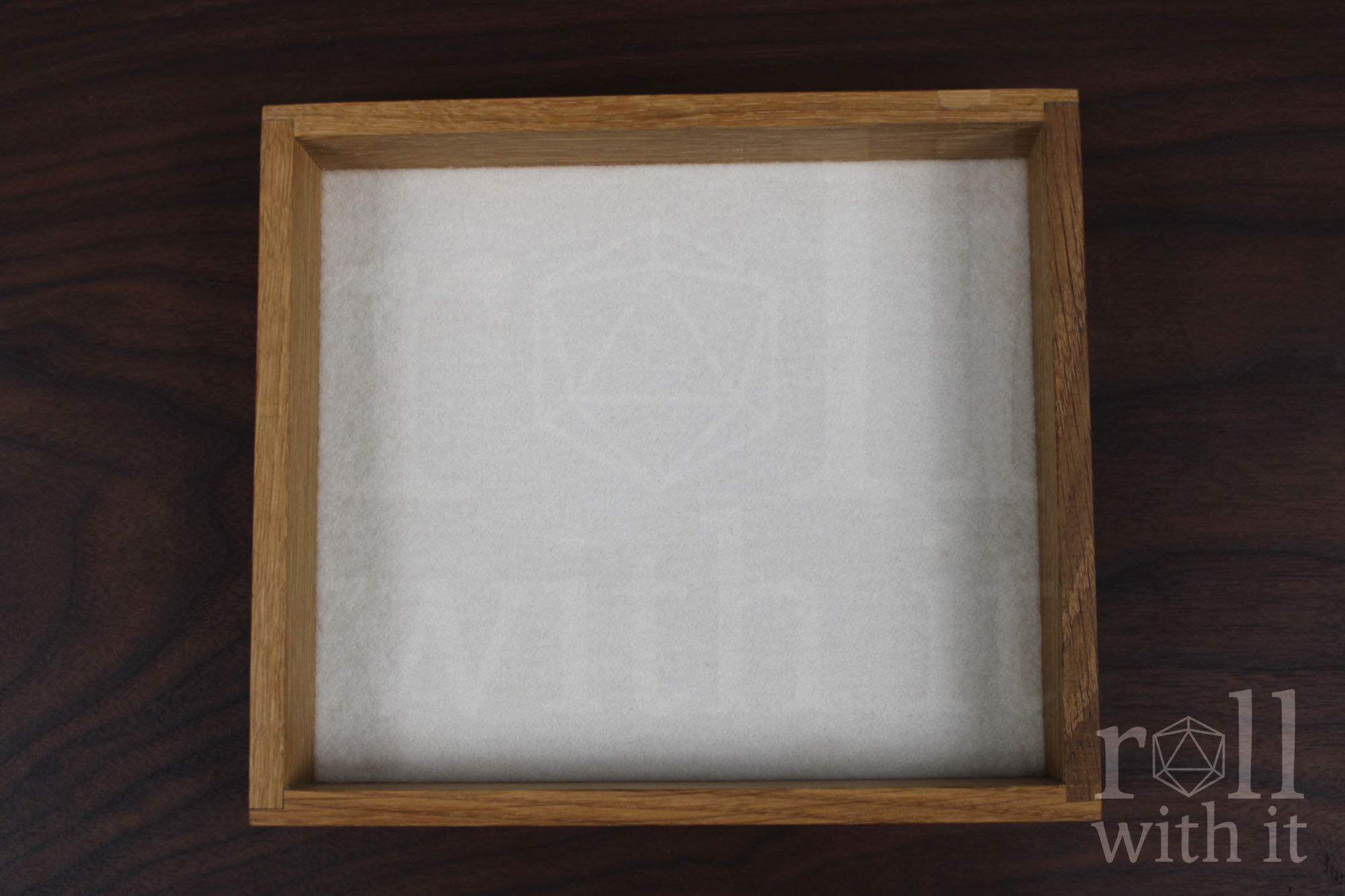 An empty dungeons and dragons tabletop dice tray with a white felt base made from white oak wood sat on a wooden table