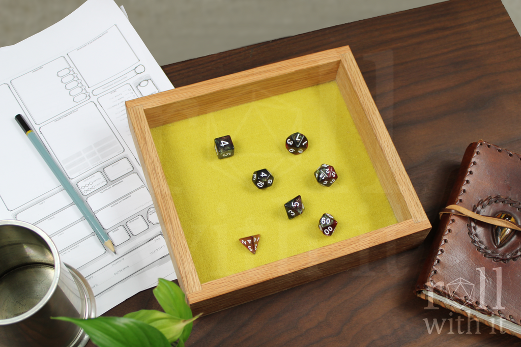 Wooden red oak dice tray with a set of red and black roleplaying dice on a chartreuse yellow felt base. The box sits on a wooden table. A character sheet and other tabletop accessories are in the background.