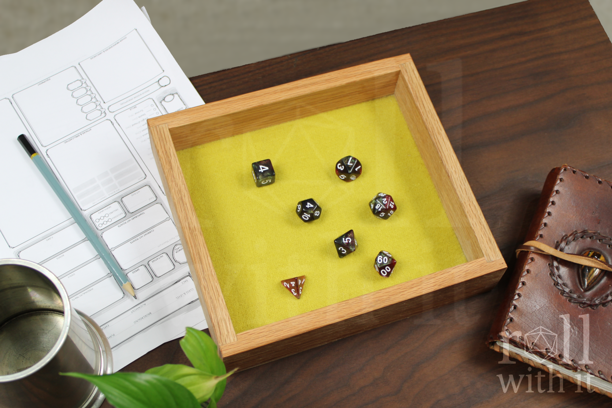 Wooden red oak dice tray with a set of red and black roleplaying dice on a chartreuse yellow felt base. The box sits on a wooden table. A character sheet and other tabletop accessories are in the background.