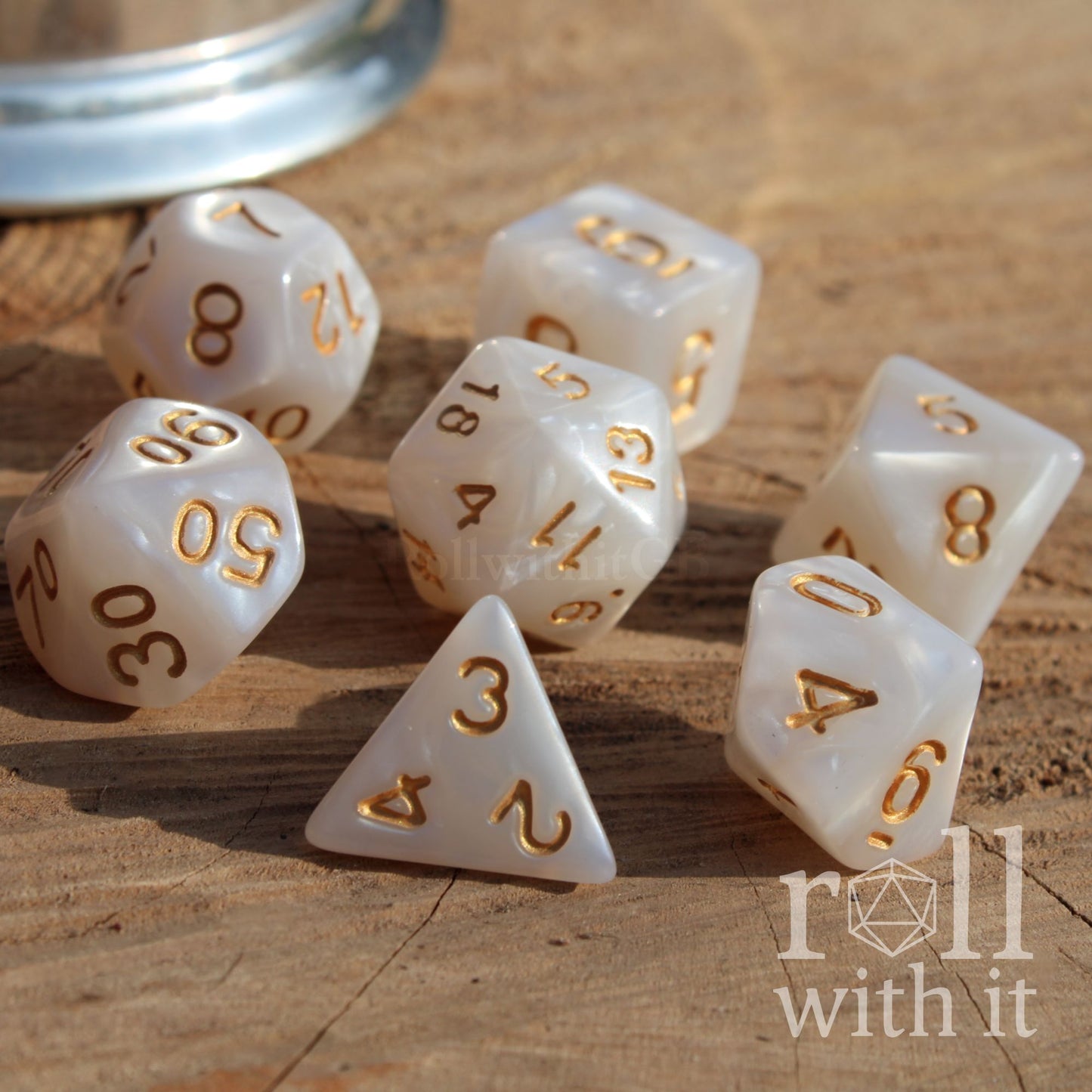 Set of white polyhedral dice with gold numbers on a wooden surface, featuring the 'roll with it' logo.