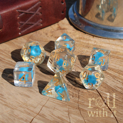Clear cute miniature blue whale dice with golden numbers on a wooden surface, featuring the 'roll with it' logo.