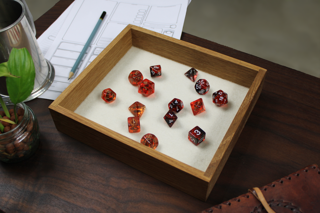 Red, orange and black dungeons and dragons roleplaying dice set in a square solid white oak RPG dice tray that has a cream white wool felt base.