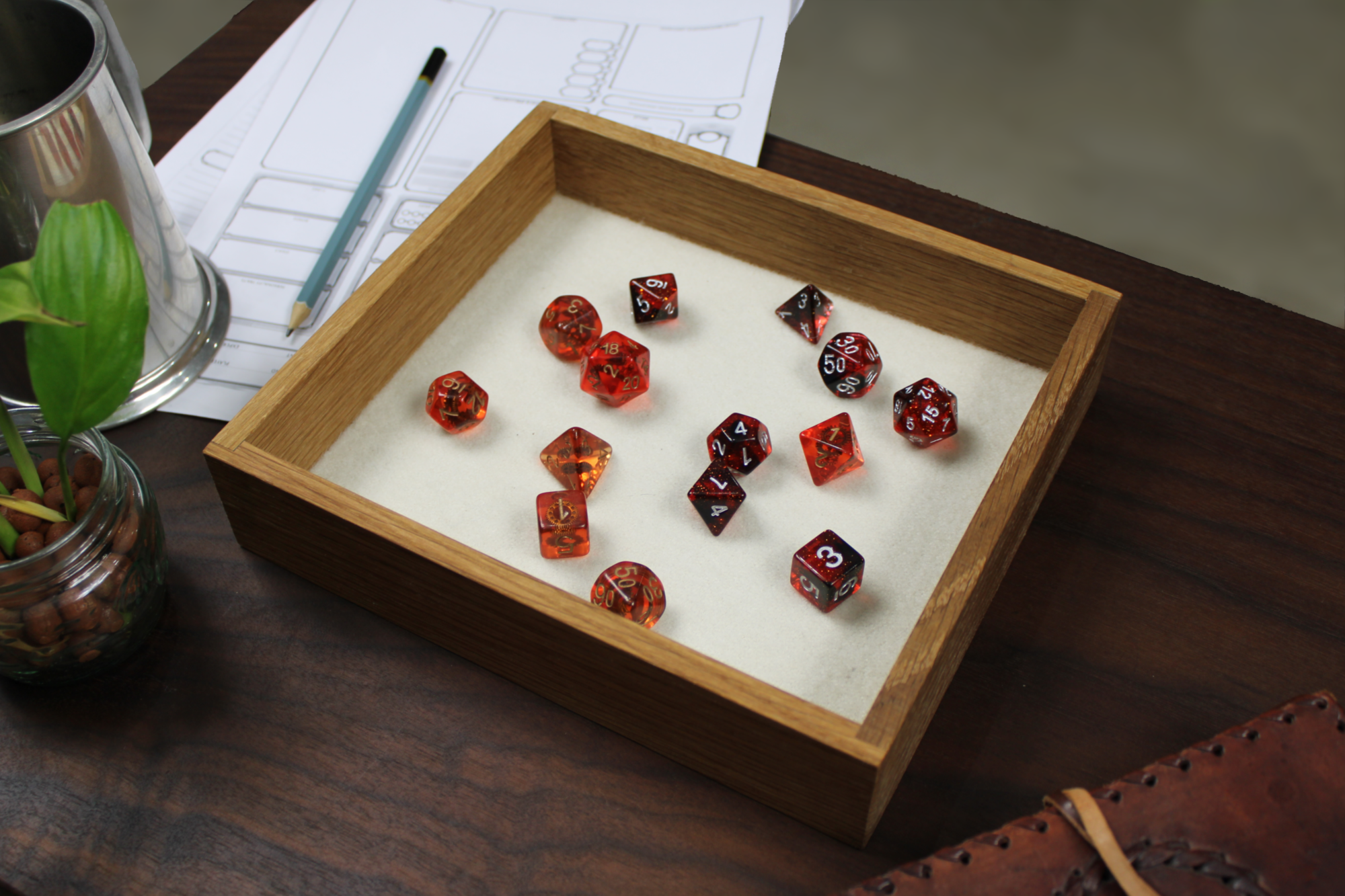 Red, orange and black dungeons and dragons roleplaying dice set in a square solid white oak RPG dice tray that has a cream white wool felt base.