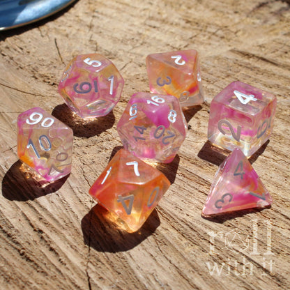 Set of colorful pink sapphic orange polyhedral dice on a wooden surface with 'roll with it' text.