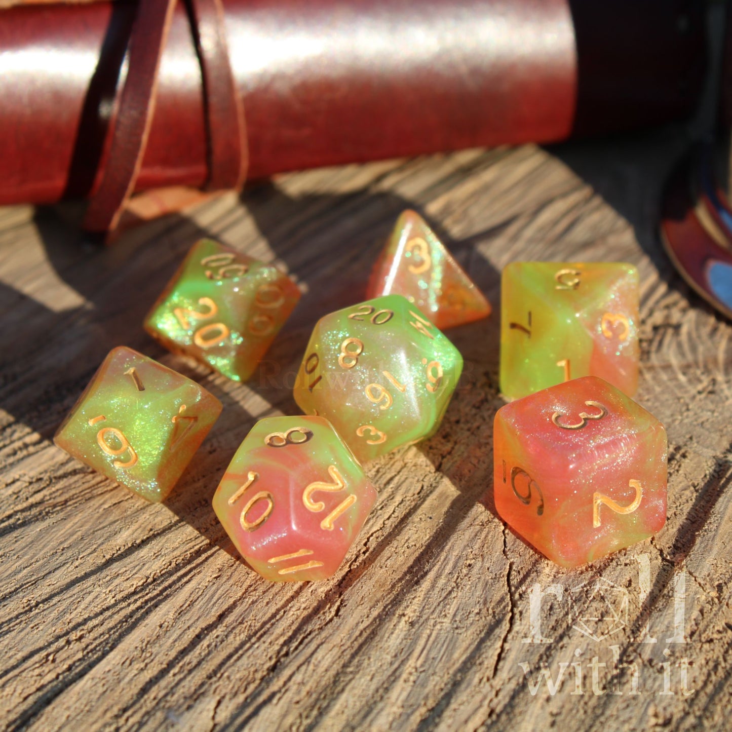 Set of colorful glitter filled spring green yellow and peach pink mxied polyhedral dice on a wooden surface with a leather-bound book in the background.